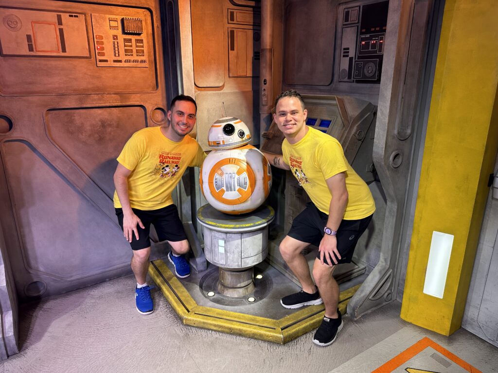 Two men posing with BB-8 in Hollywood Studios at Star Wars Launch Bay in Disney World.