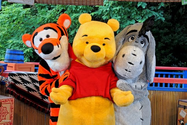 Tigger, Pooh Bear, and Eeyore posing for a photo in front of the Many Adventures of Winnie the Pooh Attraction.